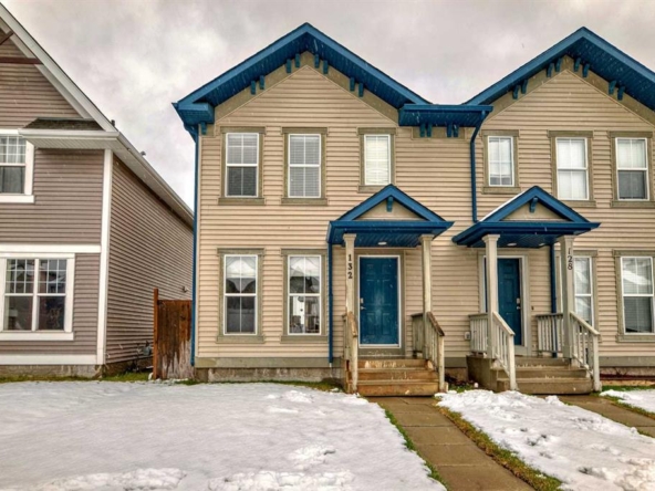 Two-story duplex home with beige siding, blue trim, matching front doors, and snow-covered front yard.