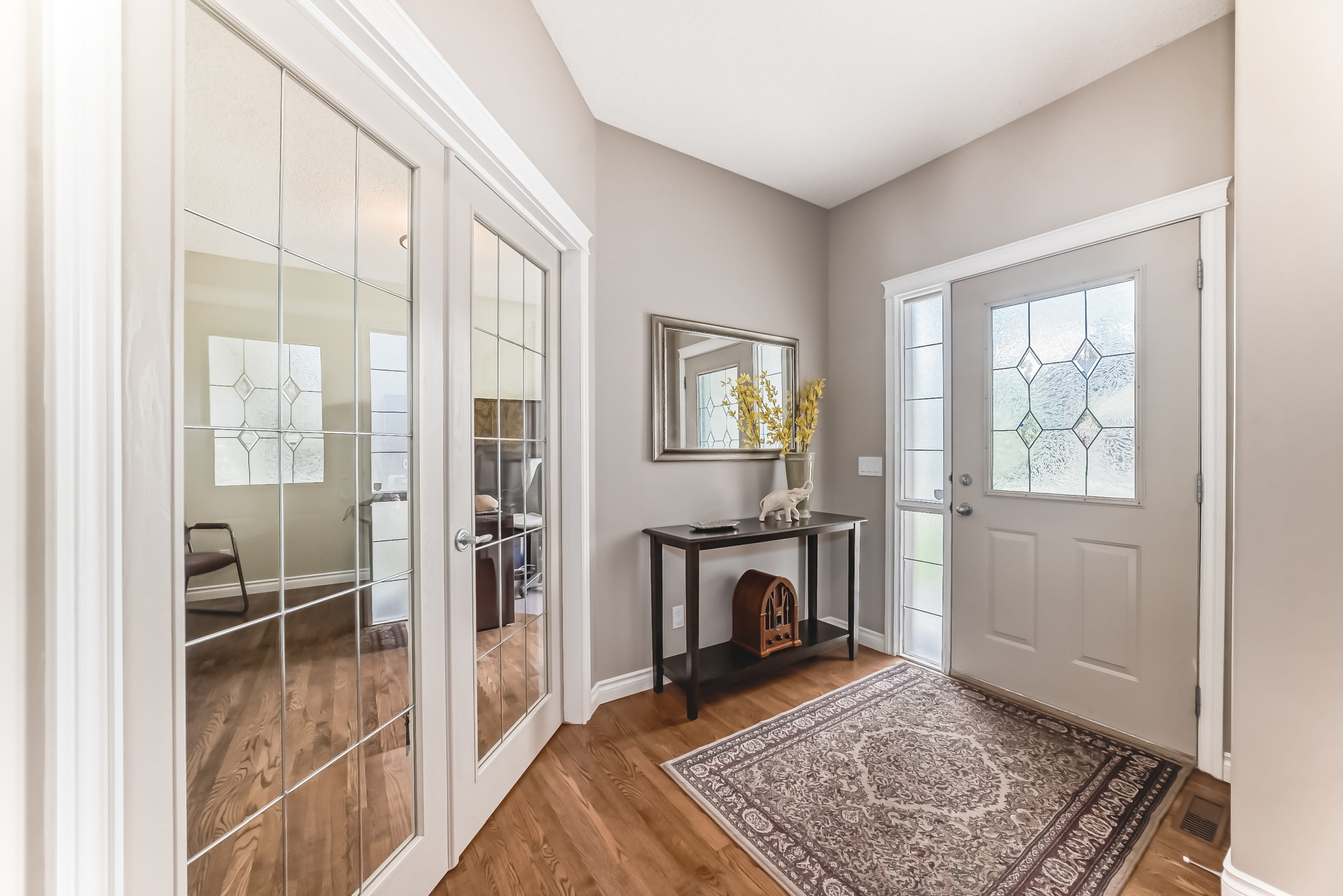 Bright front entryway with decorative glass door, mirrored closet doors, hardwood flooring, and accent table with décor.