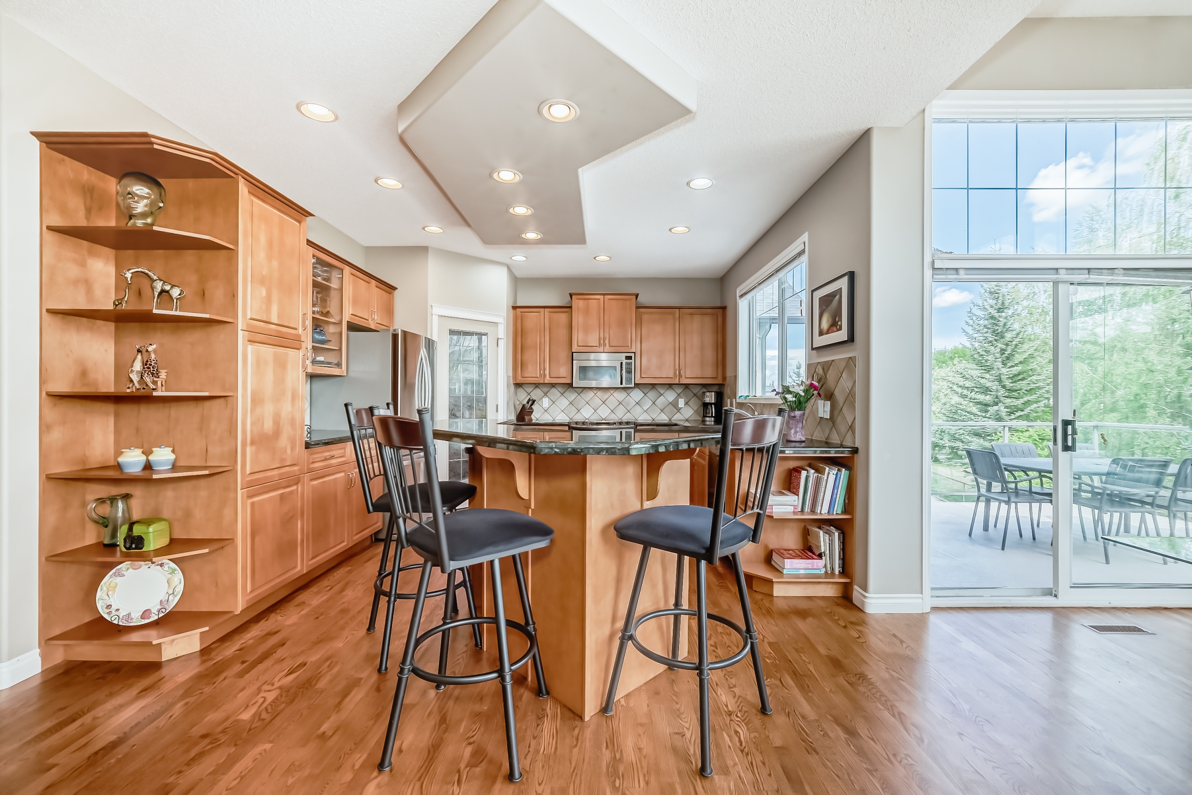 Open kitchen with breakfast bar seating, wooden cabinetry, hardwood floors, and sliding glass doors to backyard patio.
