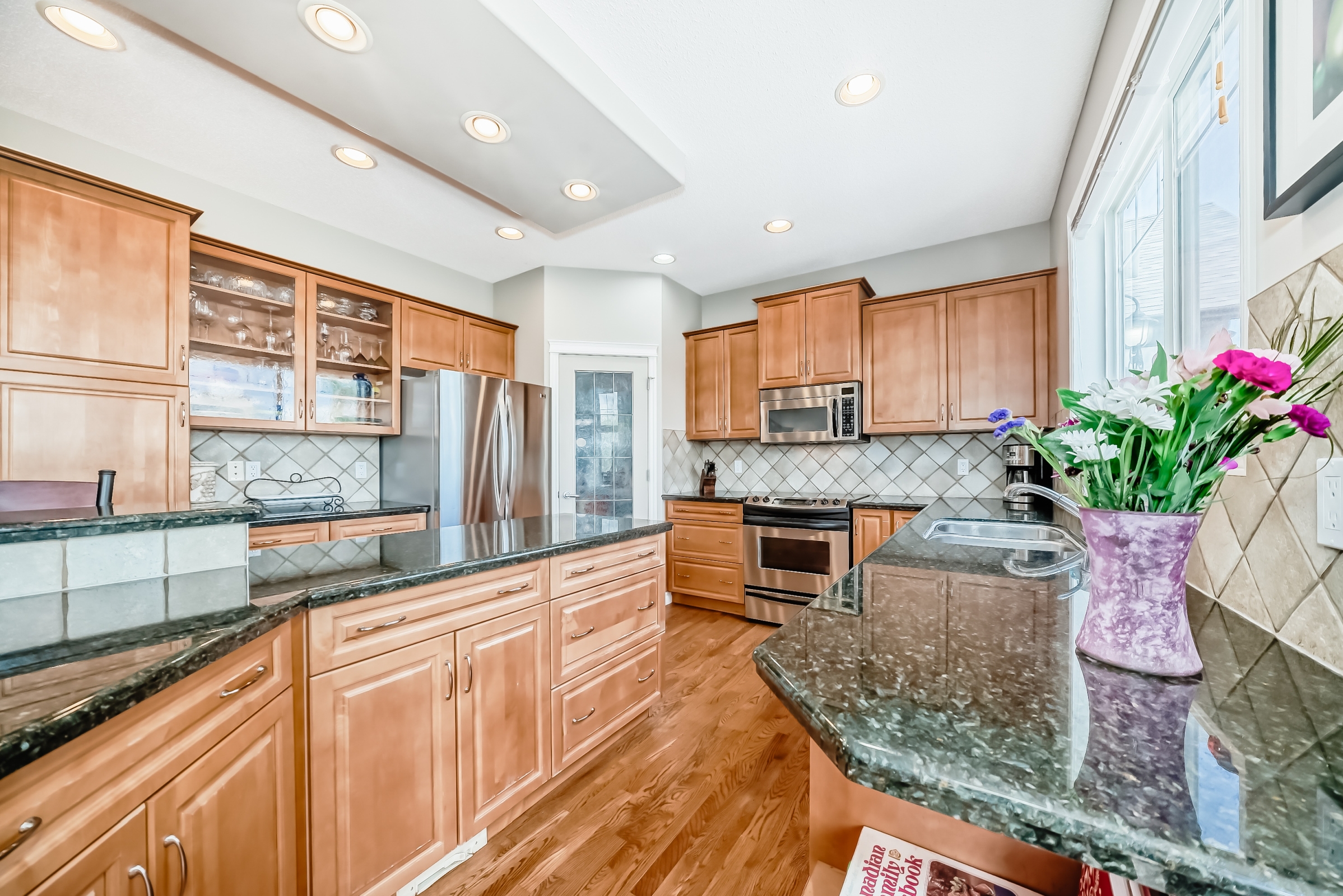 Modern kitchen with granite countertops, wooden cabinets, stainless steel appliances, and flower vase on island.