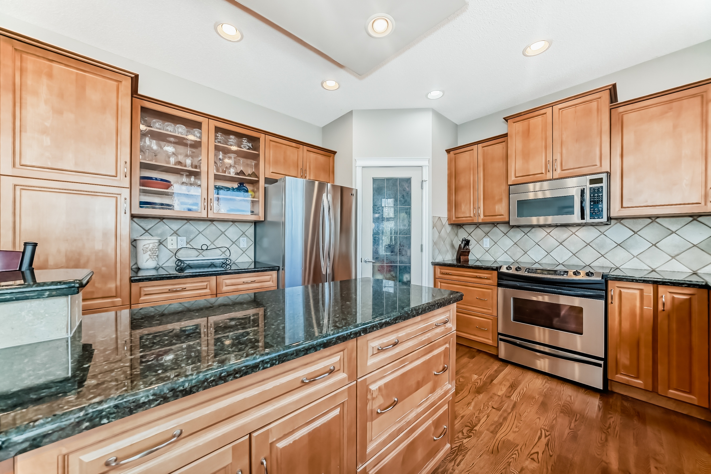 Modern kitchen with wooden cabinets, granite countertops, stainless steel appliances, and center island with hardwood flooring.
