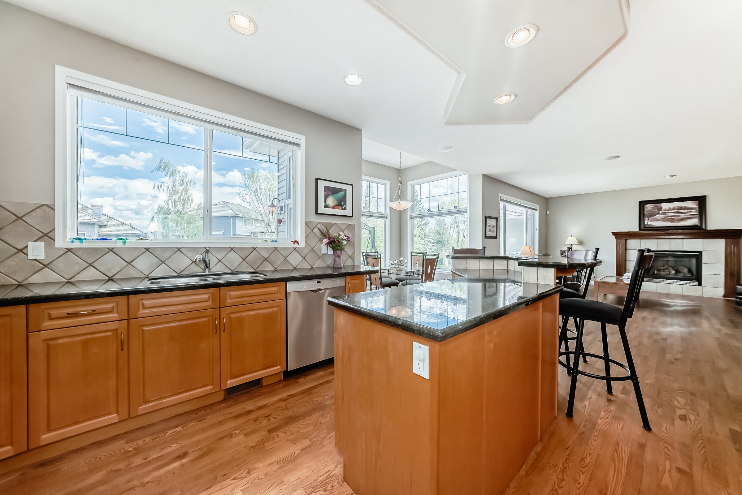 Spacious kitchen with granite island, wooden cabinets, stainless steel appliances, and open view to dining and living area.