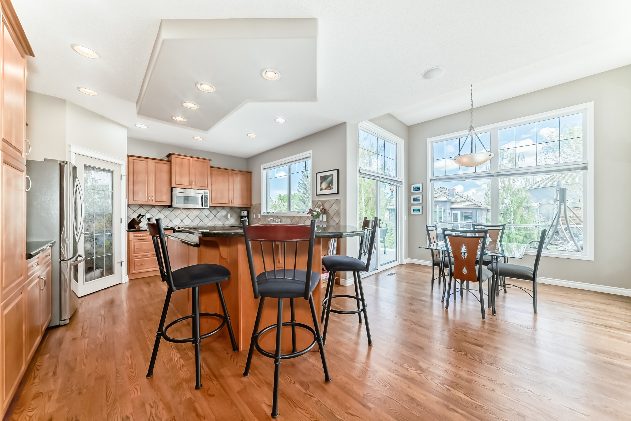Open-concept kitchen and dining area with hardwood floors, breakfast bar seating, large windows, and natural light throughout.